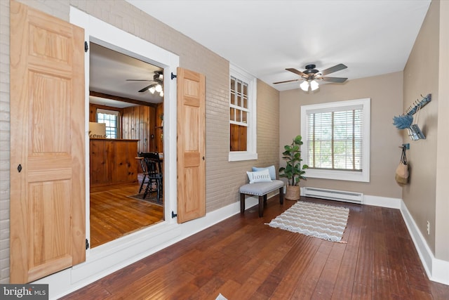 interior space with a baseboard radiator, dark wood-type flooring, ceiling fan, and brick wall