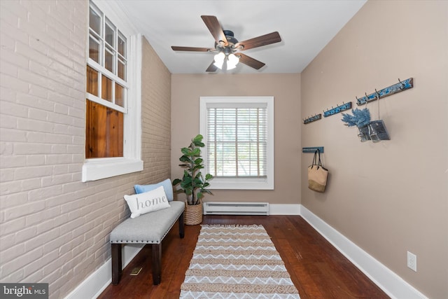 sitting room with a baseboard radiator, dark wood-type flooring, ceiling fan, and brick wall