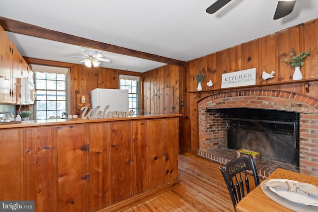 kitchen with beamed ceiling, light hardwood / wood-style flooring, a brick fireplace, white appliances, and wood walls