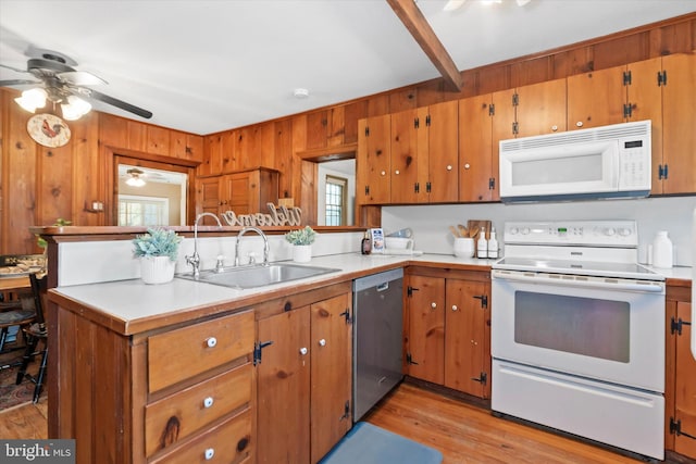 kitchen featuring kitchen peninsula, light wood-type flooring, sink, wooden walls, and white appliances