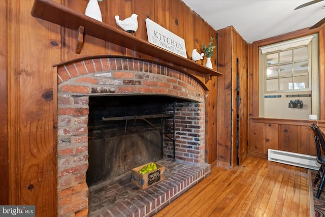 interior details with a baseboard radiator, a fireplace, wood-type flooring, and wood walls