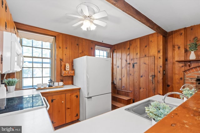 kitchen with white appliances, sink, ceiling fan, wooden walls, and beam ceiling