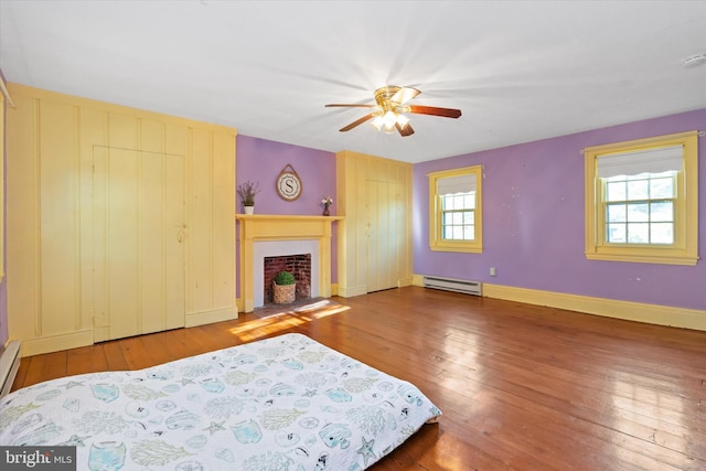 bedroom with ceiling fan, multiple windows, baseboard heating, and hardwood / wood-style floors