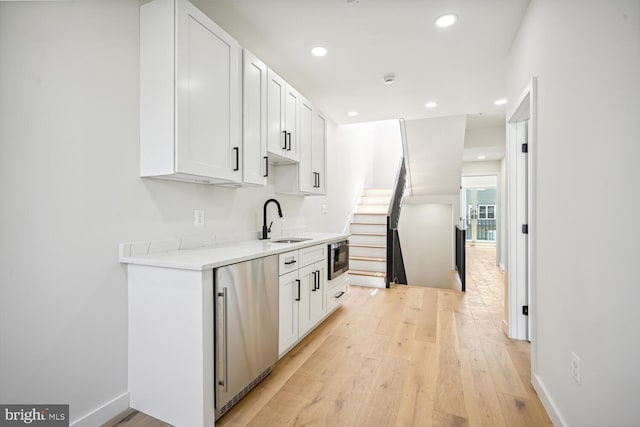 kitchen with white cabinetry, light hardwood / wood-style flooring, sink, and dishwasher