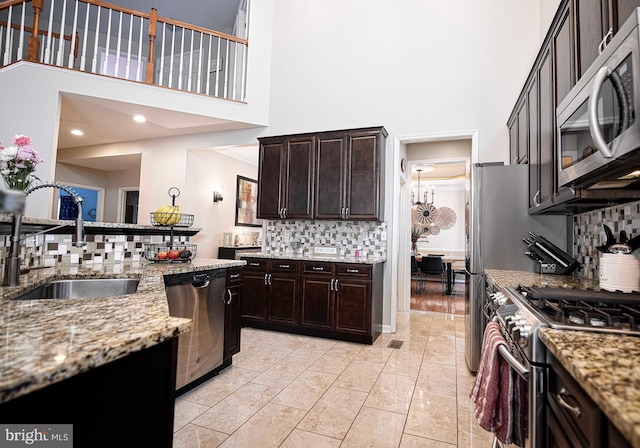 kitchen featuring light stone countertops, a towering ceiling, sink, dark brown cabinets, and stainless steel appliances