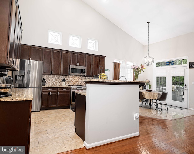 kitchen with light hardwood / wood-style floors, stainless steel appliances, a center island with sink, pendant lighting, and high vaulted ceiling