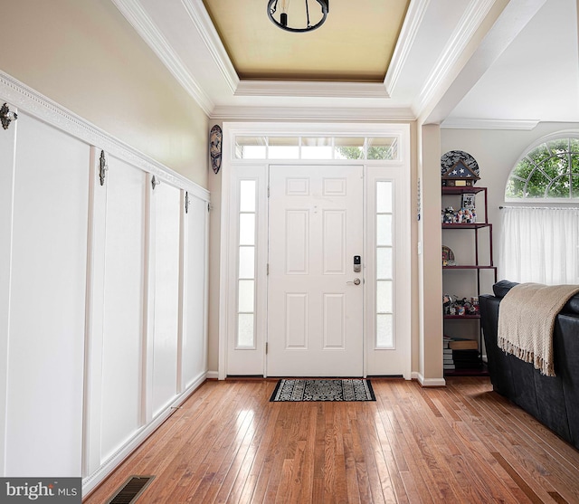 foyer featuring crown molding, light hardwood / wood-style flooring, and a tray ceiling