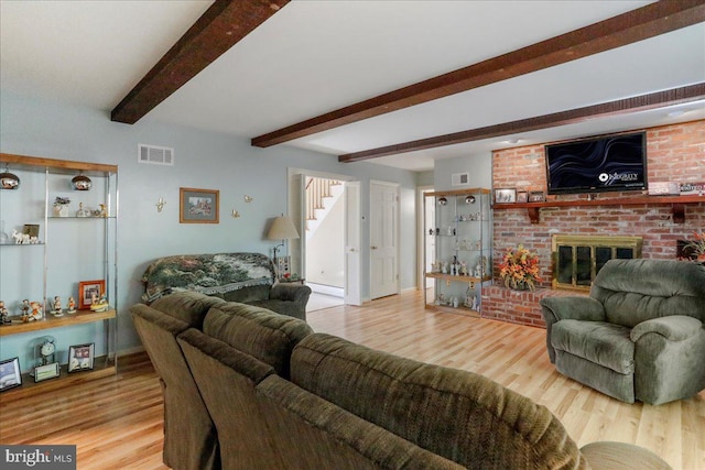 living room with a brick fireplace, hardwood / wood-style flooring, and beamed ceiling