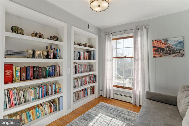 sitting room with built in features, wood walls, light hardwood / wood-style floors, and a baseboard heating unit