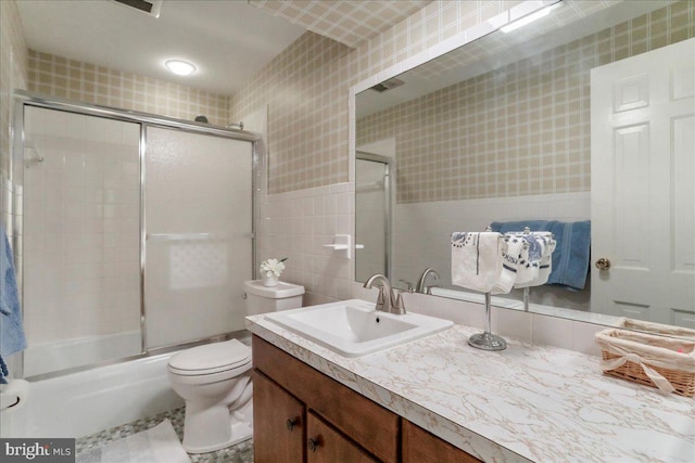 full bathroom with tile walls, enclosed tub / shower combo, toilet, and vanity