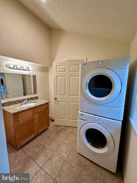 clothes washing area with a sink, stacked washer / dryer, laundry area, a textured ceiling, and light tile patterned flooring