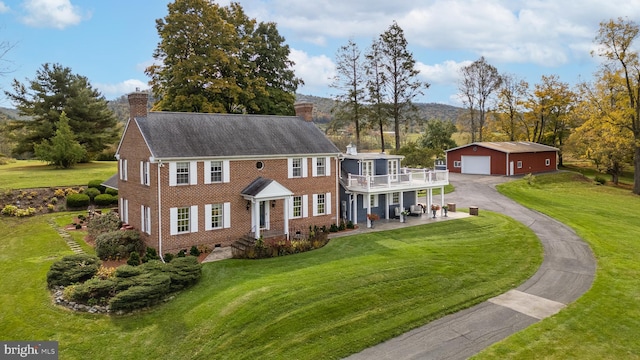 colonial-style house featuring a balcony, a garage, an outdoor structure, and a front lawn