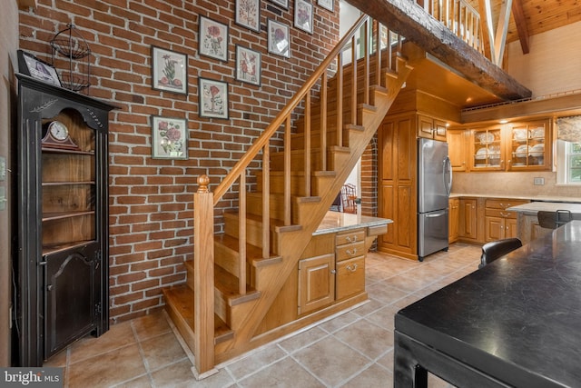 staircase featuring beamed ceiling, tile patterned flooring, a towering ceiling, and brick wall