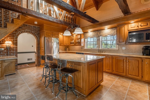 kitchen with pendant lighting, sink, a kitchen island, brick wall, and appliances with stainless steel finishes