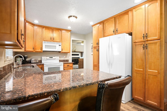 kitchen featuring a breakfast bar, dark stone countertops, light hardwood / wood-style floors, sink, and white appliances