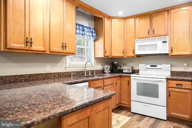 kitchen with white appliances, sink, light wood-type flooring, a textured ceiling, and dark stone countertops