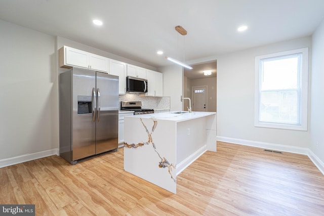 kitchen with pendant lighting, sink, appliances with stainless steel finishes, white cabinetry, and a center island with sink