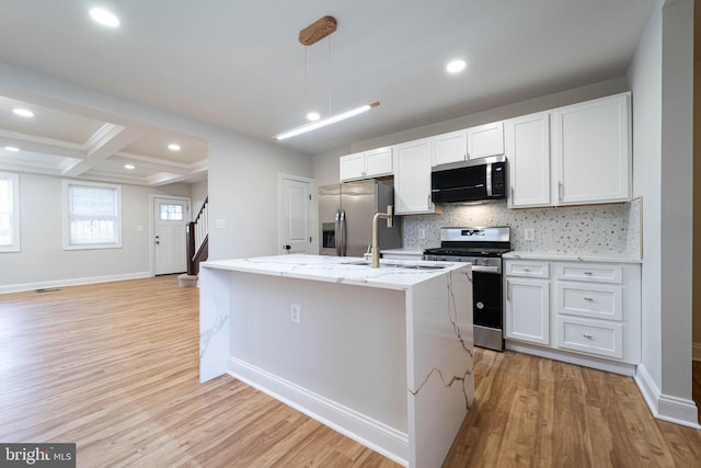 kitchen featuring light stone countertops, stainless steel appliances, an island with sink, and white cabinets