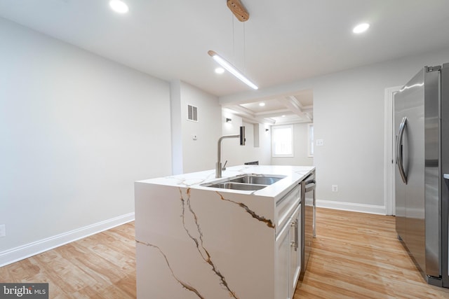 kitchen with appliances with stainless steel finishes, sink, a kitchen island with sink, light stone counters, and light hardwood / wood-style floors