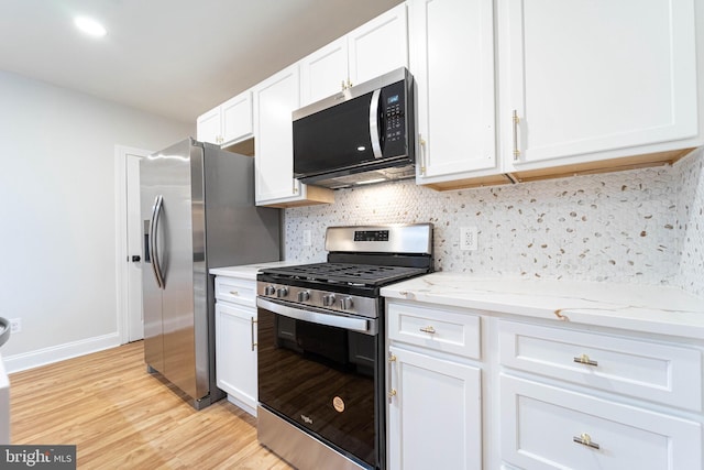 kitchen with white cabinetry, light stone counters, light wood-type flooring, stainless steel appliances, and backsplash