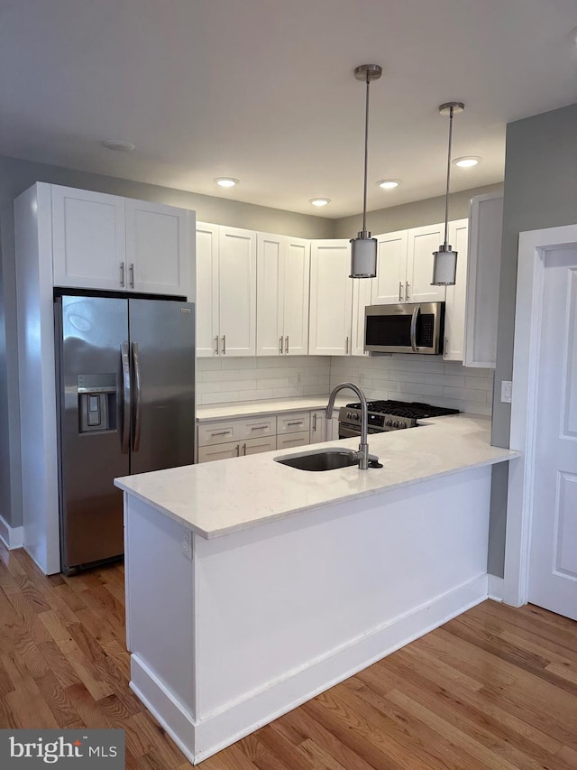 kitchen with light hardwood / wood-style flooring, sink, white cabinetry, appliances with stainless steel finishes, and decorative light fixtures