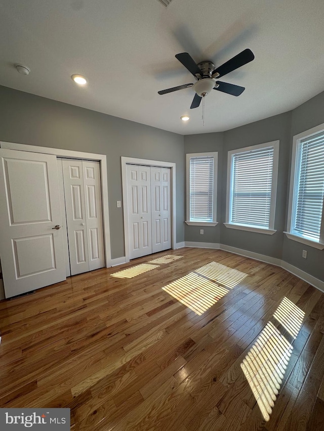 unfurnished bedroom featuring hardwood / wood-style floors, ceiling fan, and multiple closets