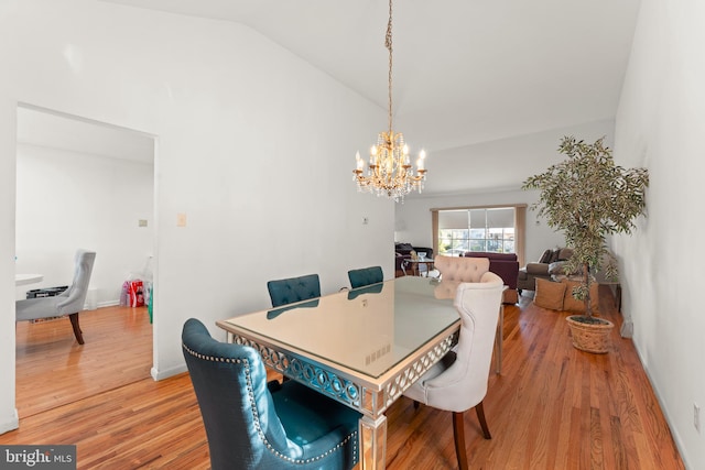 dining space featuring wood-type flooring, a notable chandelier, and vaulted ceiling