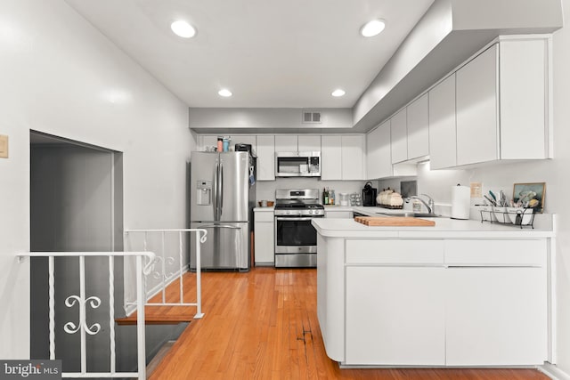 kitchen with sink, kitchen peninsula, white cabinetry, stainless steel appliances, and light hardwood / wood-style floors