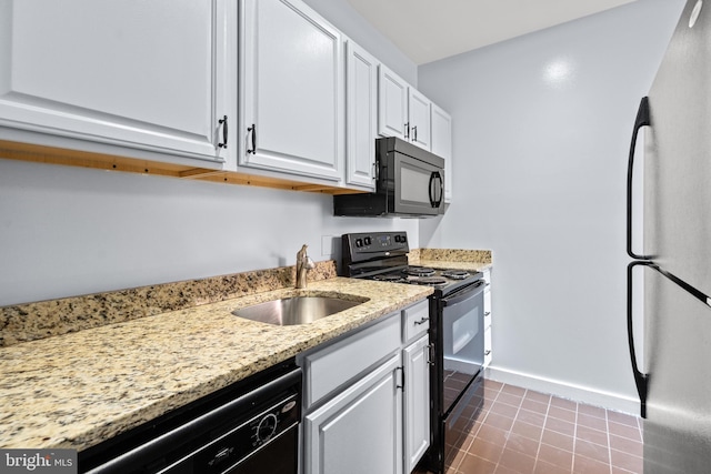 kitchen with light stone counters, black appliances, sink, tile patterned floors, and white cabinetry