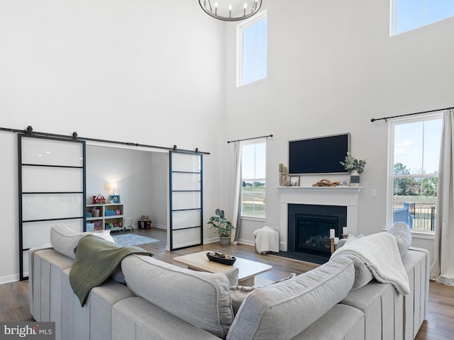 living room with a towering ceiling, a barn door, hardwood / wood-style floors, and an inviting chandelier