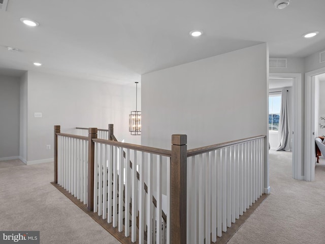 hall with light colored carpet and an inviting chandelier