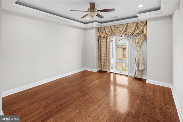 empty room with ornamental molding, ceiling fan, dark wood-type flooring, and a tray ceiling