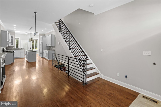 stairway featuring an inviting chandelier, hardwood / wood-style flooring, crown molding, and sink