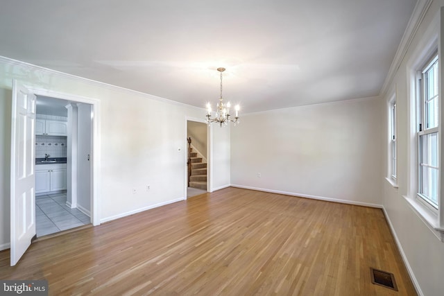 unfurnished room with light hardwood / wood-style floors, crown molding, a wealth of natural light, and a notable chandelier