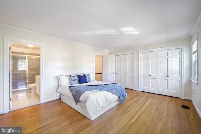 bedroom with ensuite bath, light hardwood / wood-style floors, two closets, and ornamental molding