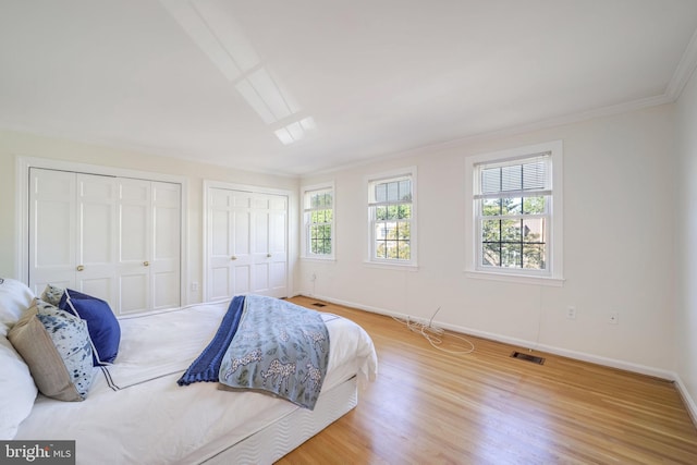 bedroom with multiple closets, crown molding, and light wood-type flooring