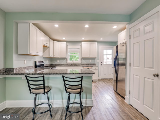 kitchen featuring kitchen peninsula, dark stone countertops, white cabinetry, and appliances with stainless steel finishes