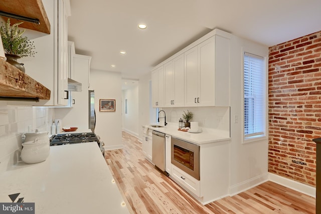 kitchen featuring tasteful backsplash, appliances with stainless steel finishes, light hardwood / wood-style flooring, and white cabinets