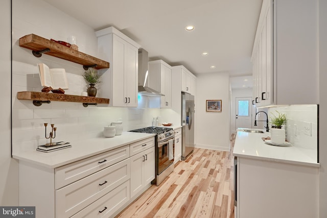 kitchen featuring sink, light wood-type flooring, stainless steel appliances, wall chimney exhaust hood, and white cabinets