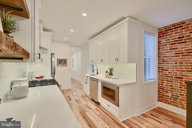 kitchen with stainless steel appliances, brick wall, sink, light wood-type flooring, and white cabinets