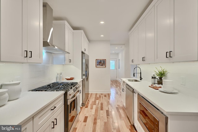 kitchen with stainless steel appliances, wall chimney exhaust hood, light hardwood / wood-style flooring, and white cabinets