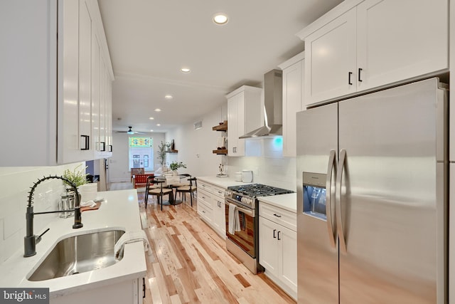 kitchen with wall chimney exhaust hood, light hardwood / wood-style flooring, sink, white cabinets, and appliances with stainless steel finishes