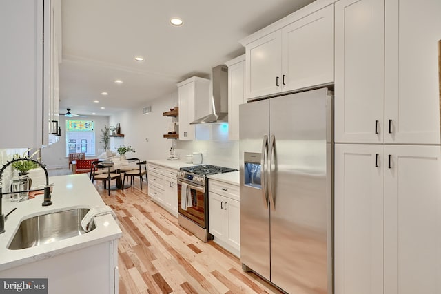 kitchen featuring appliances with stainless steel finishes, sink, light wood-type flooring, white cabinetry, and wall chimney exhaust hood