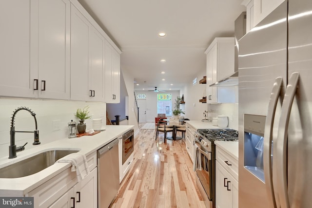 kitchen with ceiling fan, appliances with stainless steel finishes, white cabinetry, light wood-type flooring, and sink