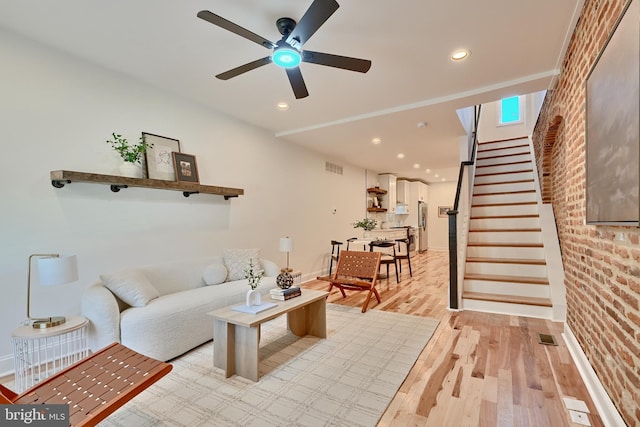 living room featuring light hardwood / wood-style flooring, brick wall, and ceiling fan