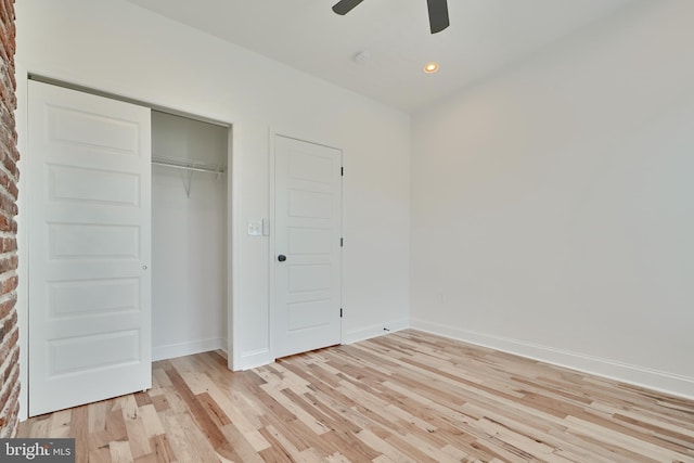 unfurnished bedroom featuring brick wall, a closet, light wood-type flooring, and ceiling fan