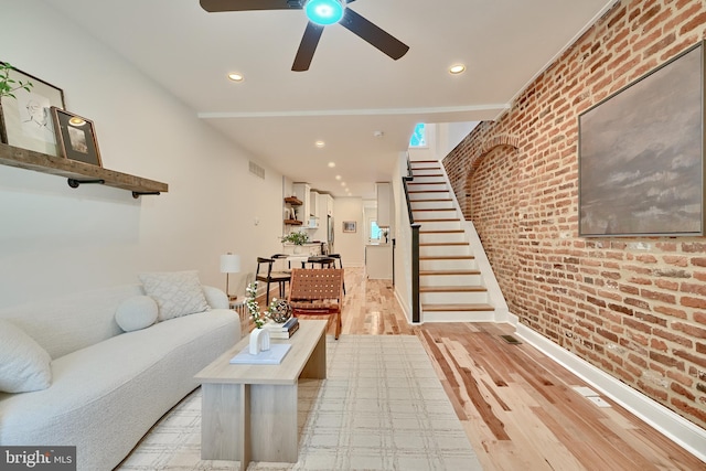 living room with brick wall, light hardwood / wood-style floors, and ceiling fan