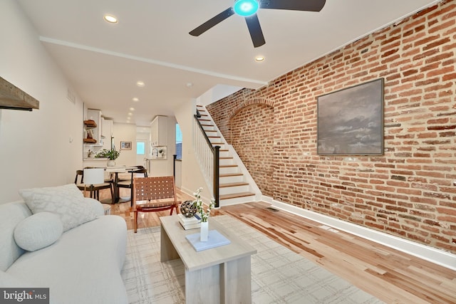 living room with light hardwood / wood-style floors, brick wall, and ceiling fan