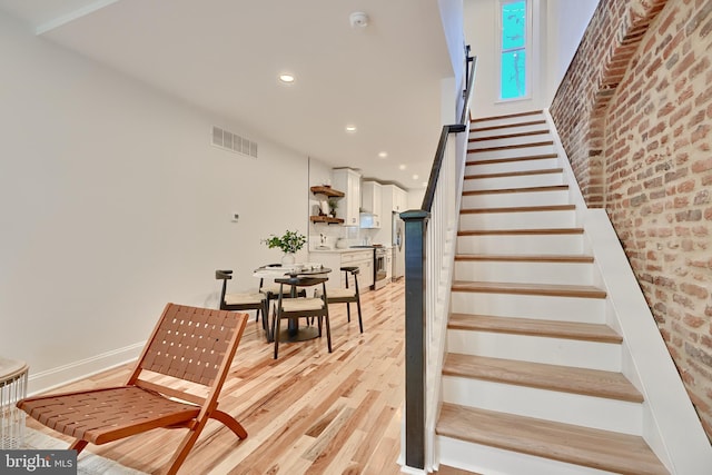 stairway featuring brick wall and hardwood / wood-style floors