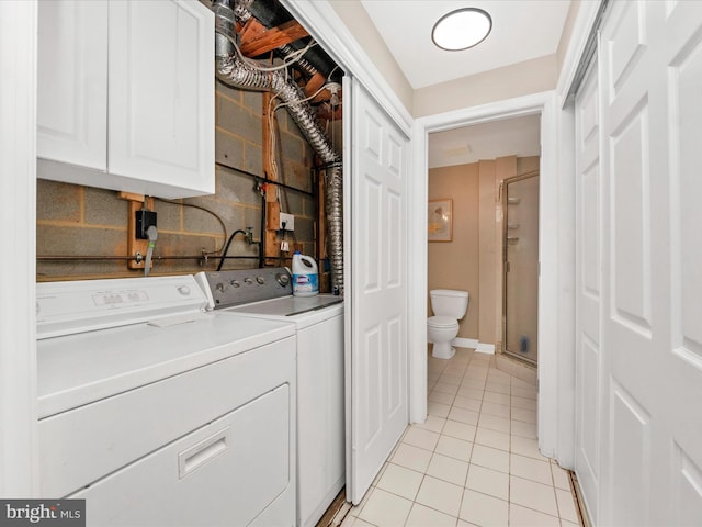 clothes washing area featuring washing machine and dryer, light tile patterned flooring, and cabinets